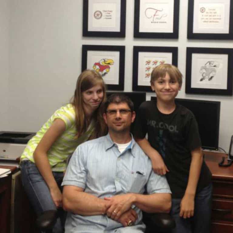 School principal at his desk with his kids standing by him.