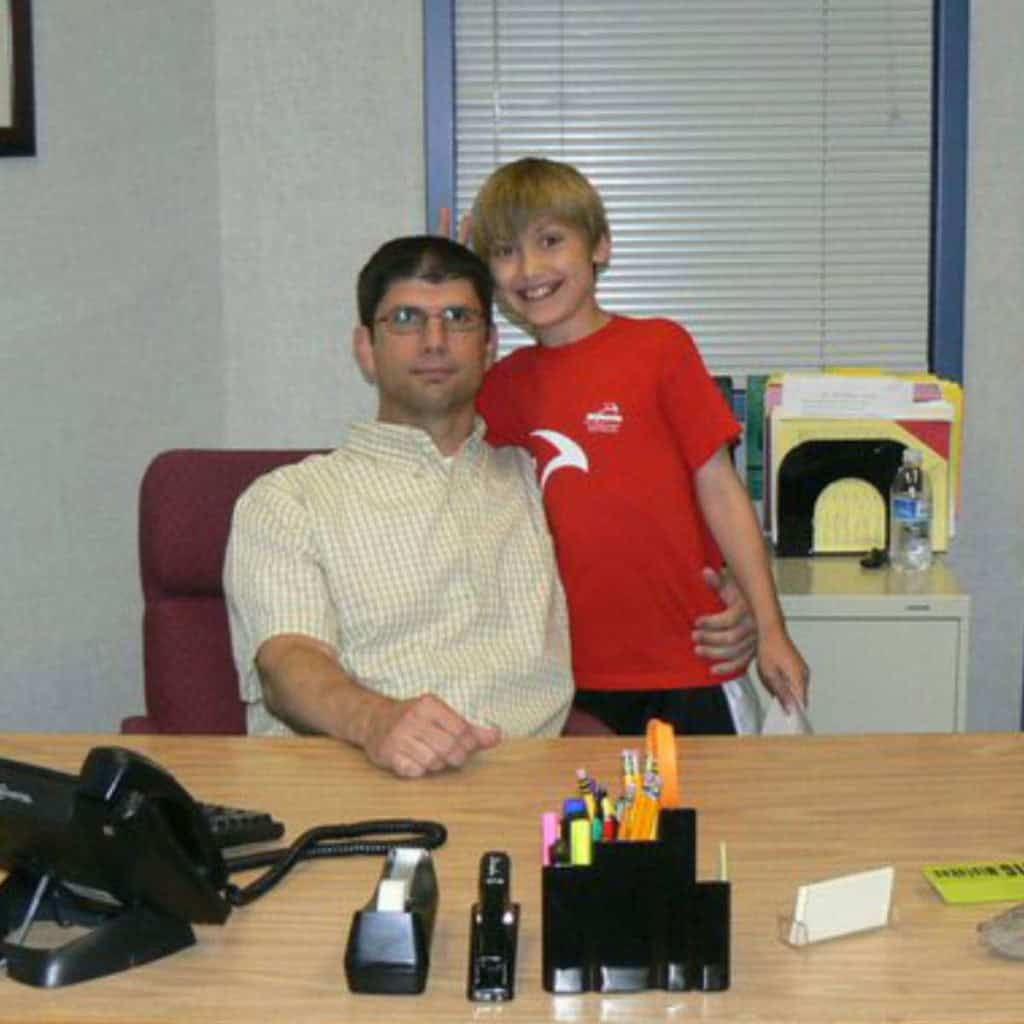 School principal at his desk with his son standing by him.