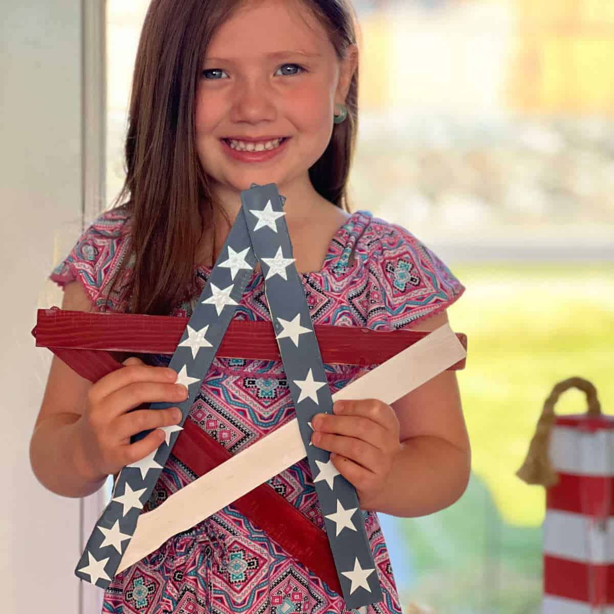 Little girl holding a patriotic star she made out of paint sticks.