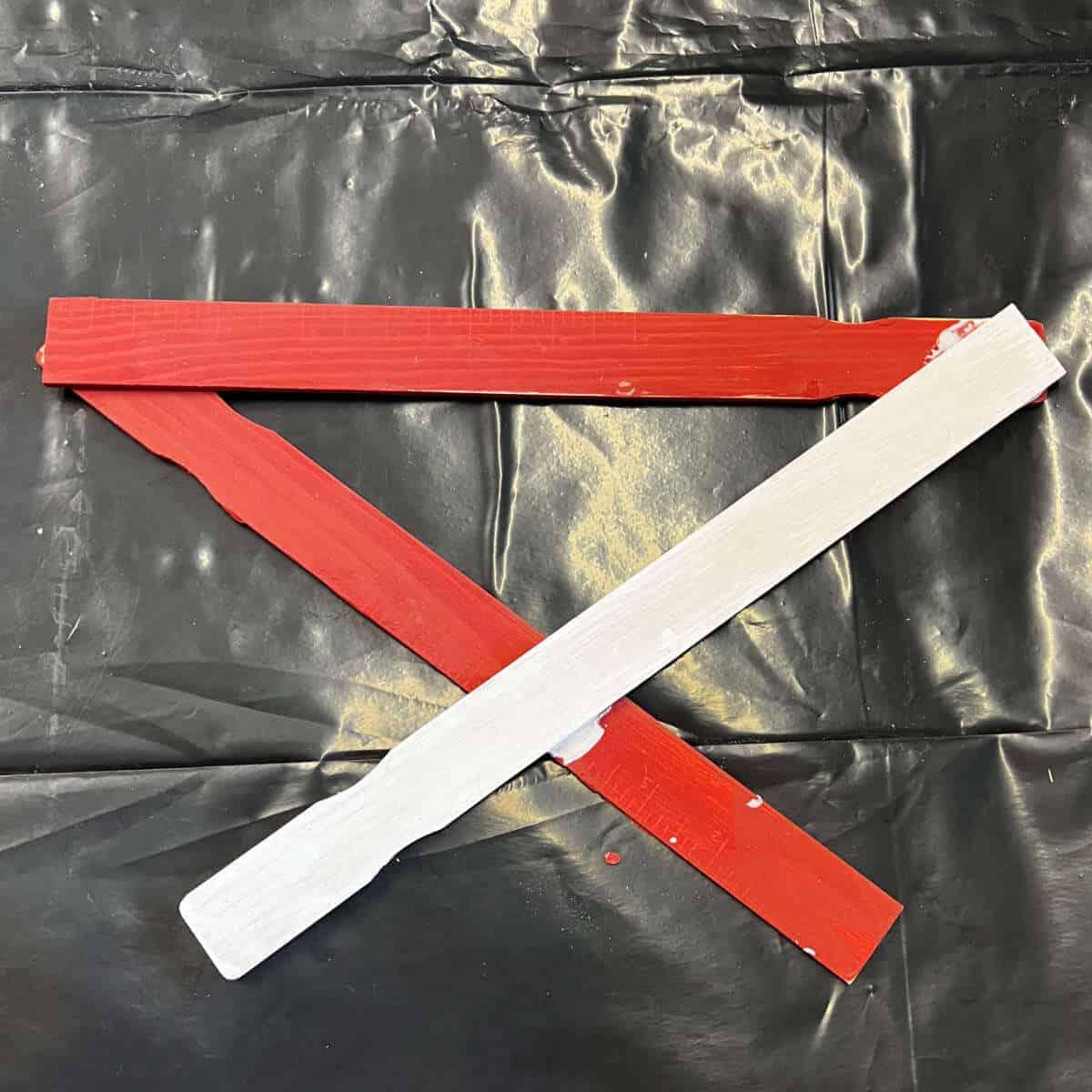 Two paint sticks painted red and one painted white glued together to start to form a star.