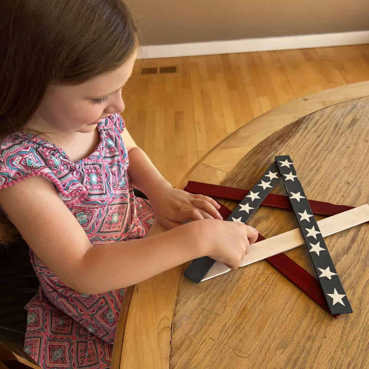 Little girl putting white vinyl star stickers on a patriotic star made out of paint sticks.