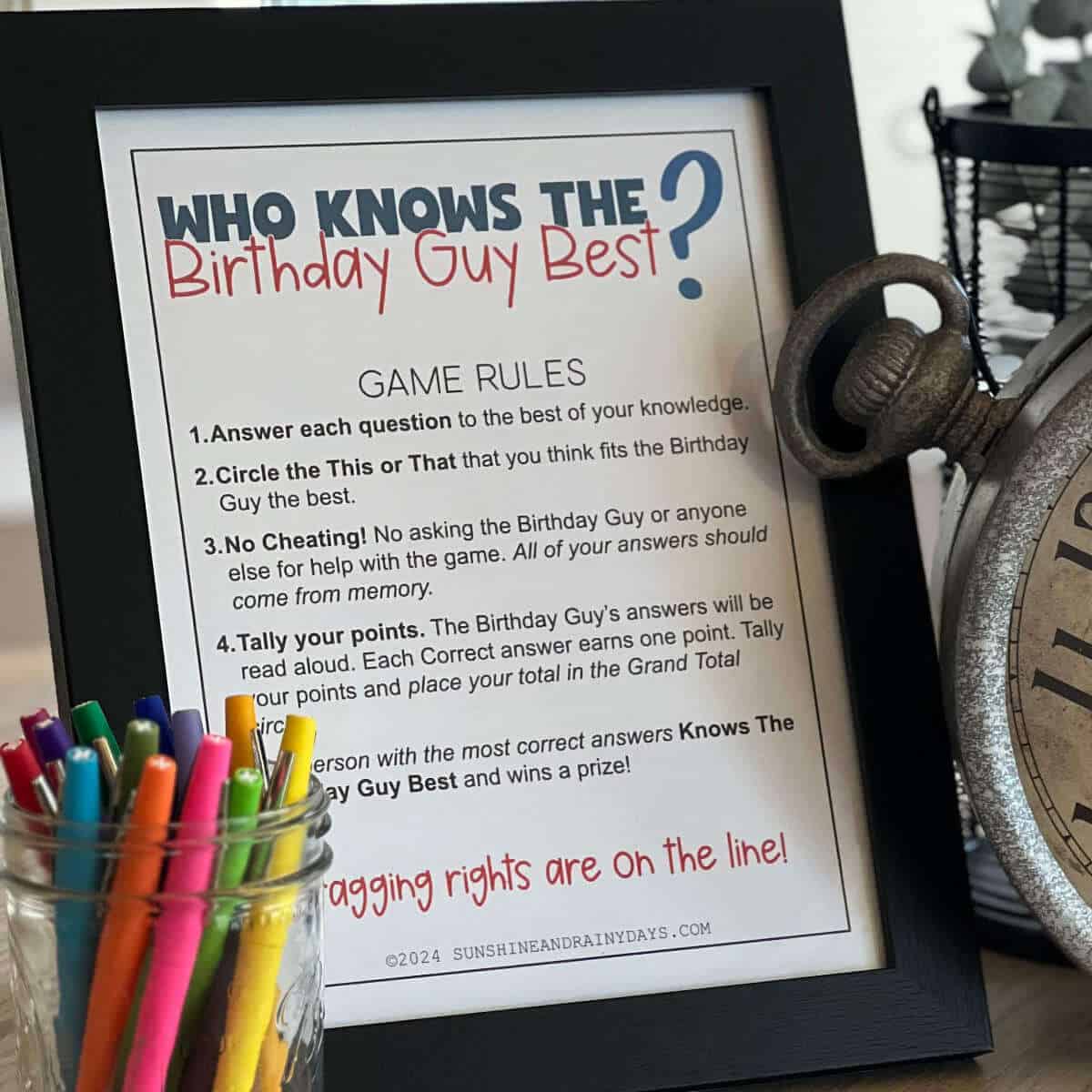 Who Knows The Birthday Guy Best Birthday party game rules framed and sitting on a table next to a jar of pens.