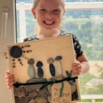 Little girl holding a family portrait made out of rocks and a wood canvas.