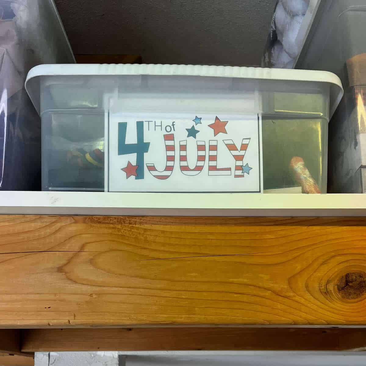 4th of July storage box label inside the front of a clear storage box that's on a shelf next to other storage boxes.