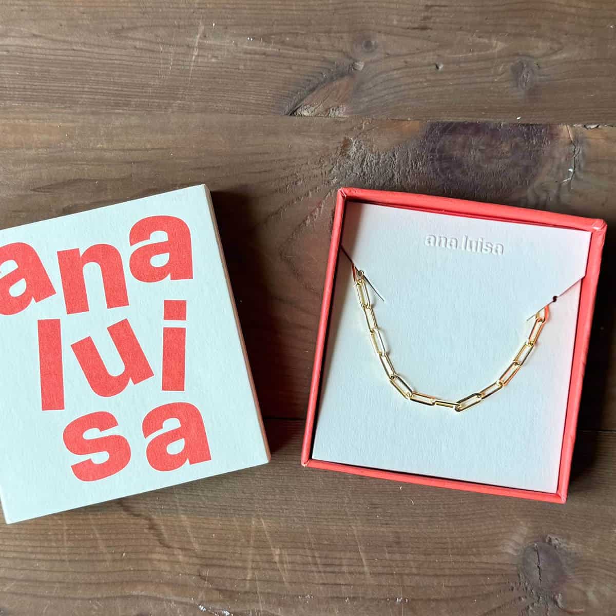 Ana Luisa paperclip necklace in a box with the cover sitting next to it.