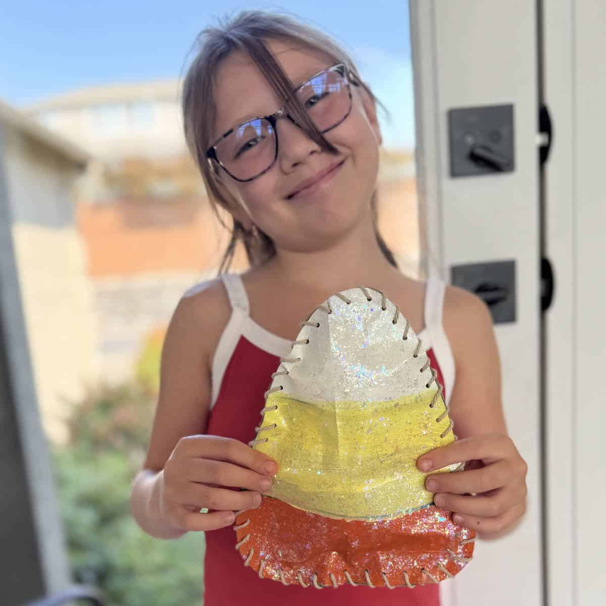 Girl standing in front of a windowed door holding a paper bag candy corn that she made.