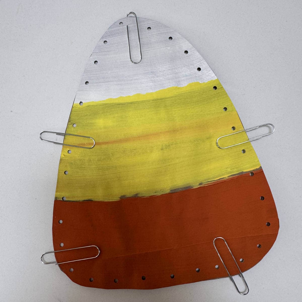 Painted brown paper bag candy corn paperclipped together with holes punched around the edges.
