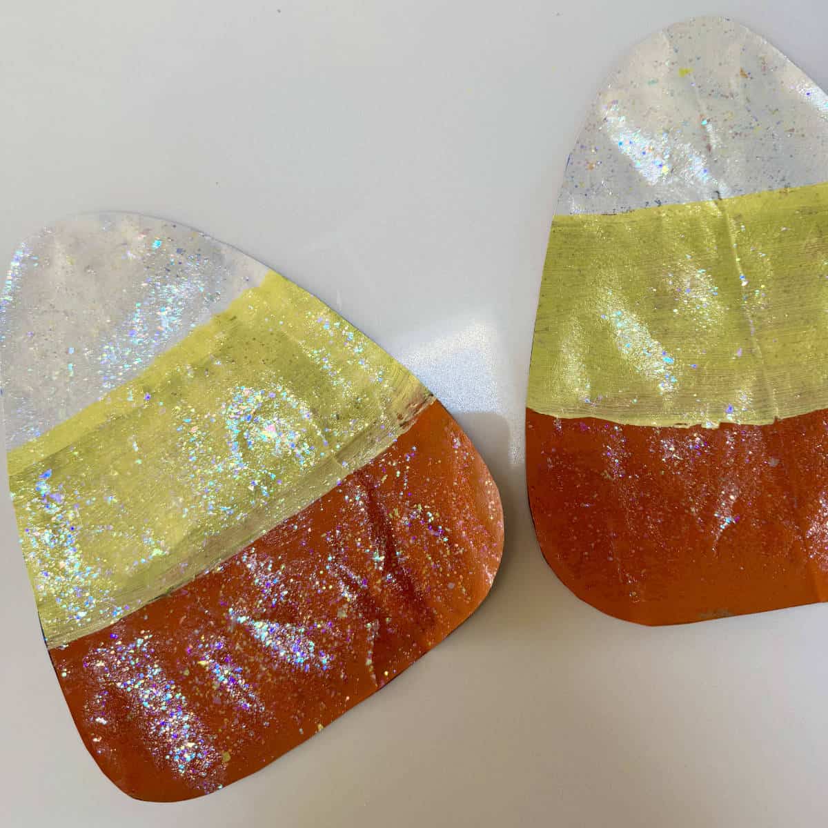 Two painted candy corn with sparkles, cut out, and laying on a counter.