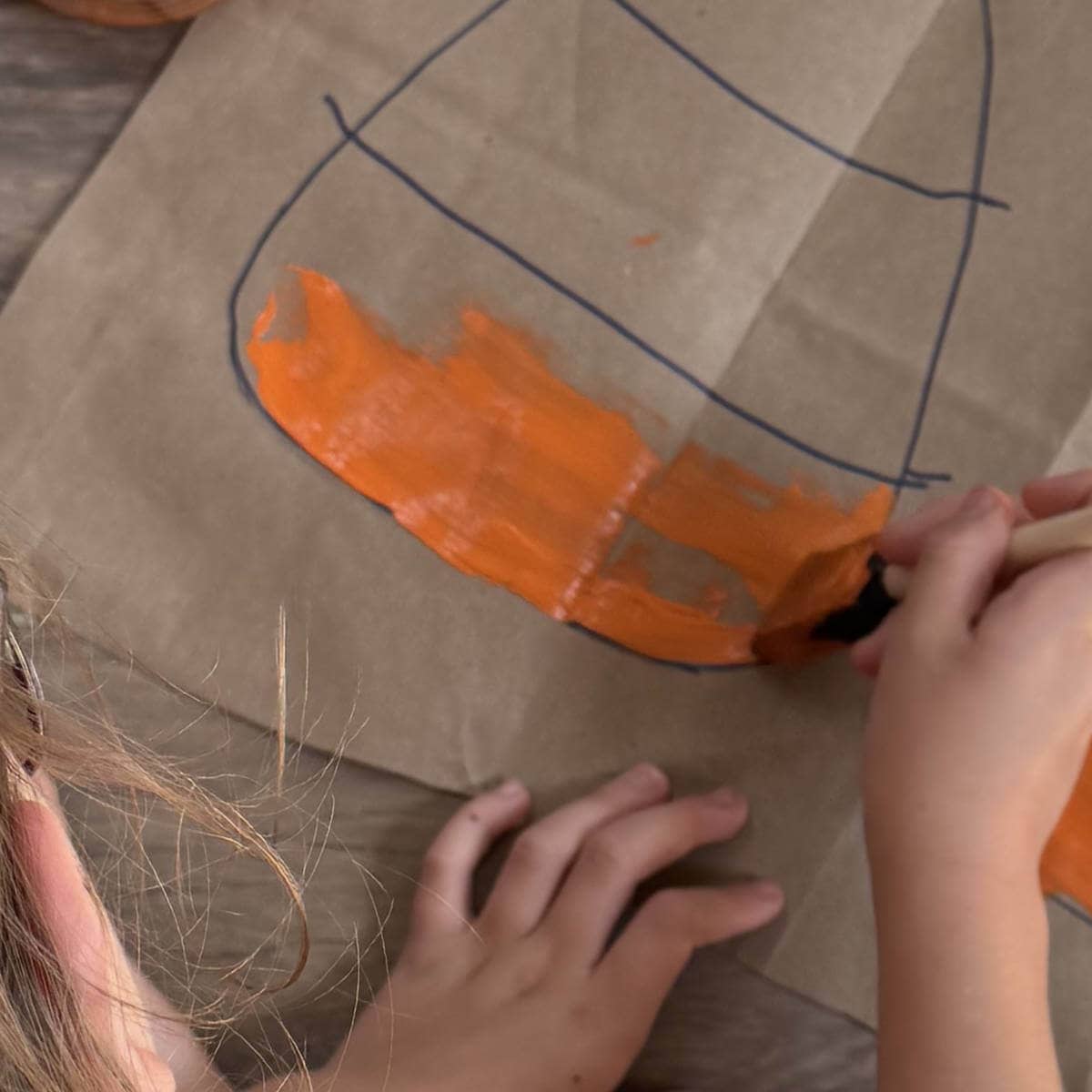 Painting orange onto the bottom portion of a candy corn that's been drawn on a brown paper bag.