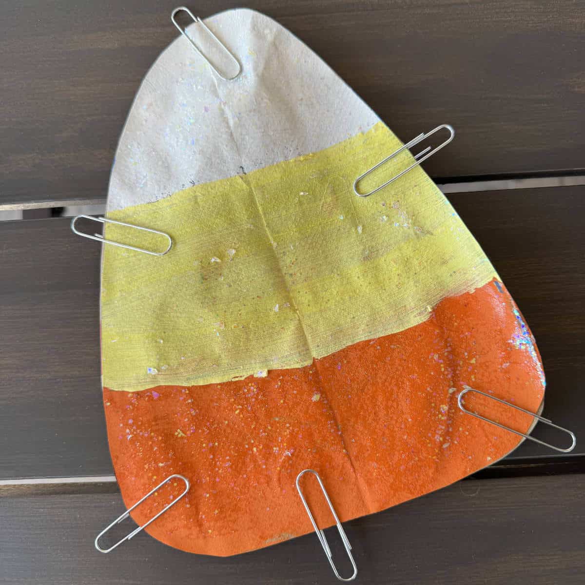 Candy corn painted on a brown paper bag with paperclips along the edges holding two pieces together.