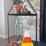 Image of a black metal log holder with fall decor on it sitting in front of the fireplace.