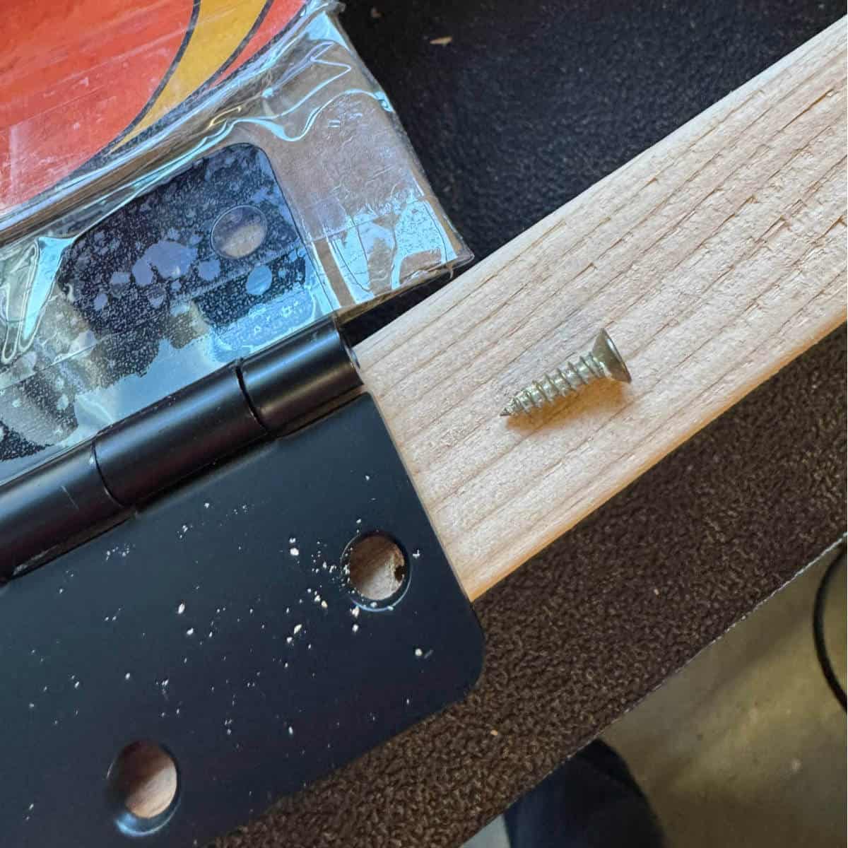 Image of a hinge taped to the bottom of a printable flame with the other half of the hinge on a 2x4.